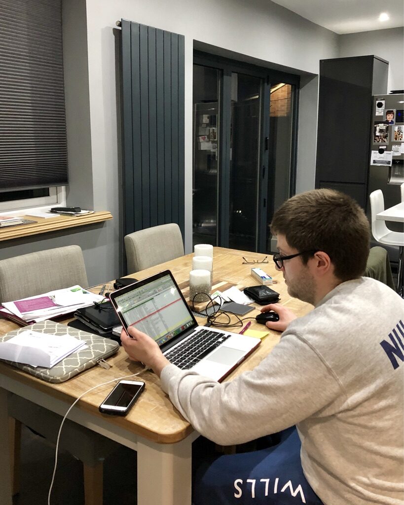 white man with dark hair and glasses sat at a dining room table working on his computer