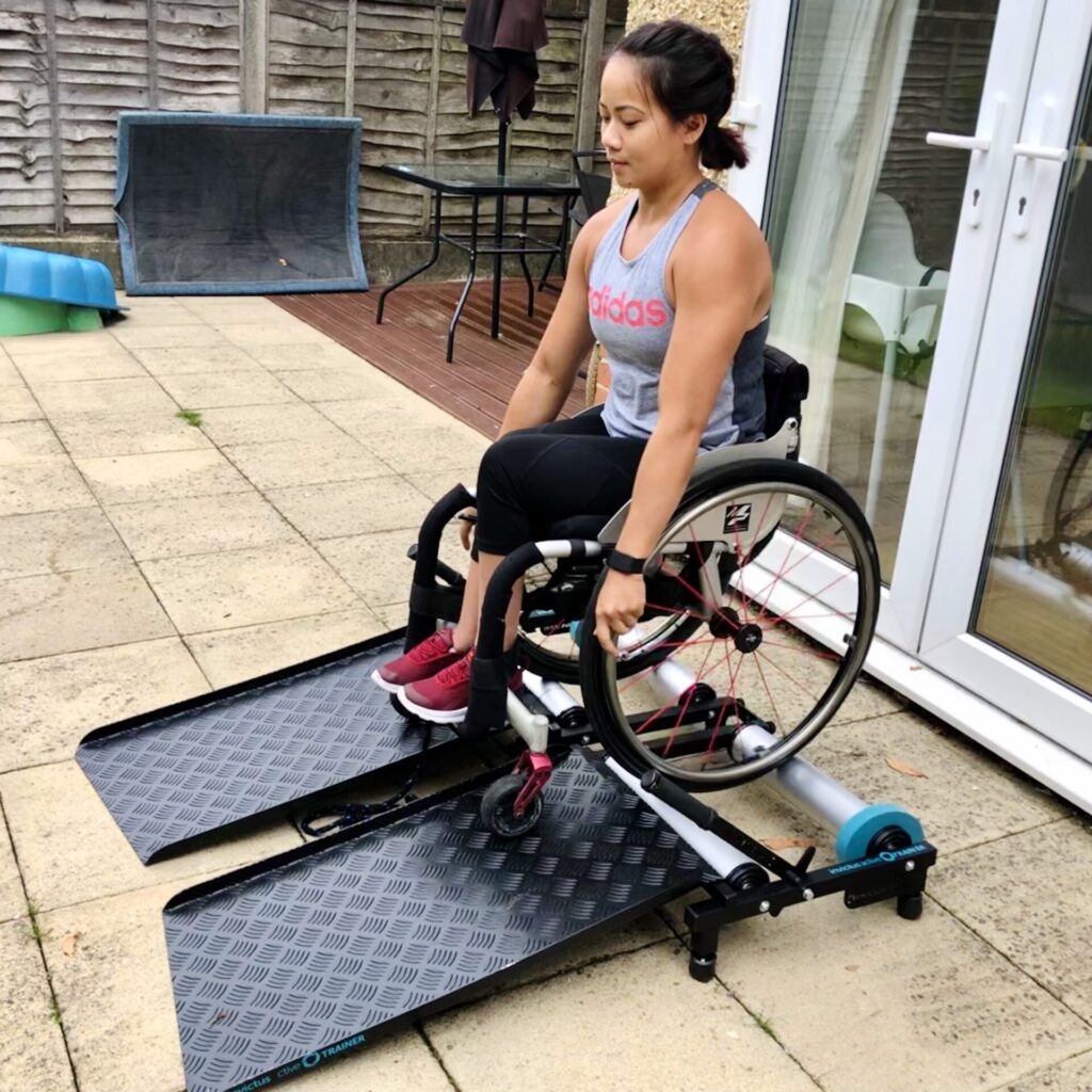 Photo of a woman in a wheelchair in the process of using an 'Invictus Active Trainer' treadmill, for wheelchair users, during a workout.