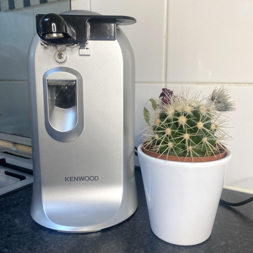 Photo of a kitchen aid. In this case, an electric can opener, with a small cactus in a pot placed next to it for scale.