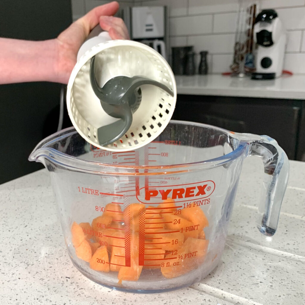Photo of a demonstration of a kitchen aid. In this case, a portable food processor is held above a glass litre sized measuring jug of pre-cut carrots.